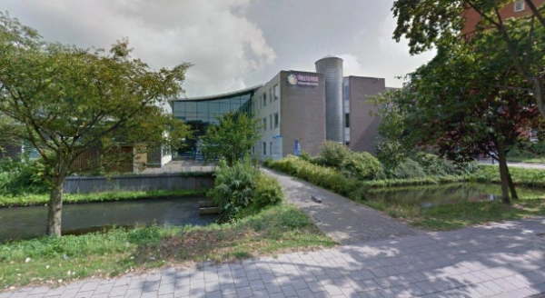 Vooraanzicht van het Cultuurhuis aan de Van Bleyswijckstraat met omliggende bomen en waterpartij.